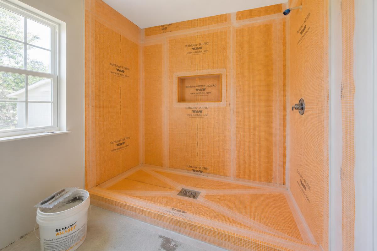 Shower alcove in an Idaho home prepped with an orange Schluter-KERDI waterproofing membrane, taped seams, KERDI-BOARD niche and bonded drain before tile